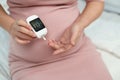 Pregnant woman holding glucose meter and checking blood sugar level by herself at home. gestational diabetes concept Royalty Free Stock Photo