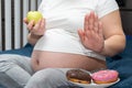 Close-up of a pregnant woman holding a green apple in her hands, refusing donuts. Healthy food during pregnancy Royalty Free Stock Photo
