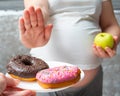 Close-up of a pregnant woman holding a green apple in her hands, refusing donuts. Healthy food during pregnancy Royalty Free Stock Photo