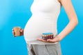 Close up of pregnant woman holding a paper cup and a heap of blisters with pills at colorful background with copy space. Treatment