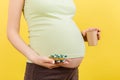 Close up of pregnant woman holding a paper cup and a heap of blisters with pills at colorful background with copy space. Treatment