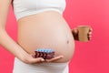 Close up of pregnant woman holding a paper cup and a heap of blisters with pills at colorful background with copy space. Treatment
