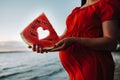 Close-up of a pregnant woman holding a piece of watermelon with a heart made with it, standing in nature