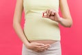 Close up of pregnant woman holding a pill in her hand against her belly at colorful background with copy space. Taking vitamins Royalty Free Stock Photo