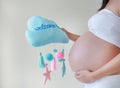 Close-up pregnant woman holding soft fabric mobile with text `Welcome Baby` at tummy