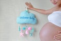 Close-up pregnant woman holding soft fabric mobile with text `Welcome Baby` at tummy