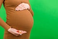 Close up of pregnant woman holding a stack of vitamin pills in her hand at colorful background with copy space. Medicine concept