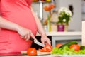 Close up pregnant woman with knife on kitchen cuts tomato