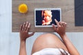 Pregnant woman looking and touching the digital tablet with the ultrasound of her baby at home