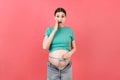 Close up of a pregnant woman in opened jeans measuring her belly with a tape measure at colorful background with copy space.