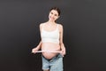 Close up of a pregnant woman in opened jeans measuring her belly with a tape measure at colorful background with copy space.