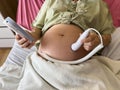 close up pregnant woman patient using fetal droppler device to listening baby heartbeat on bed in hospital