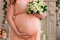 Close up of pregnant woman in a peach dress with bouquet white roses of flowers