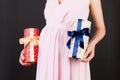 Close up of pregnant woman in pink dress holding two gift boxes at black background. Is it a boy or a girl Expecting twins. Royalty Free Stock Photo