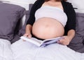 Close up pregnant woman reading a book while lying on a bed in t Royalty Free Stock Photo