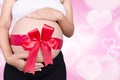 Close up pregnant woman with red ribbon gift on belly on heart b