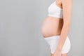 Close up of pregnant woman`s abdomen at gray background. Girl is wearing white underwear. Maternity concept. Copy space Royalty Free Stock Photo