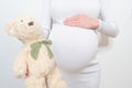 Close-up pregnant woman`s belly with teddy toy bear. Pregnancy, parenthood, preparation and expectation concept Royalty Free Stock Photo