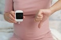 Pregnant woman showing thumb down and holding glucose meter with result of measurement sugar high level. gestational diabetes