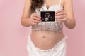 Pregnant woman showing ultrasound photo of baby on pink background Royalty Free Stock Photo
