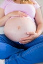 Close up of pregnant woman sitting on couch touching her belly Royalty Free Stock Photo