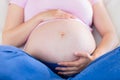 Close up of pregnant woman sitting on couch touching her belly Royalty Free Stock Photo