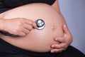 Close-up pregnant woman with stethoscope listening belly to baby Royalty Free Stock Photo