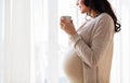 Close up of pregnant woman with tea cup at window