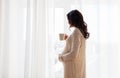 Close up of pregnant woman with tea cup at window Royalty Free Stock Photo