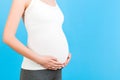 Close up of pregnant woman touching her abdomen at blue background. Future mother is wearing home clothing. Expecting of a baby. Royalty Free Stock Photo