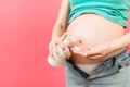 Close up of pregnant woman in unzipped jeans using moisture cream to prevent stretch marks on her belly at colorful background Royalty Free Stock Photo