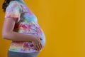 Close up of pregnant woman wearing hipster tie dye t-shirt and grey yoga pants, arms on her belly. Female hands wrapped around big Royalty Free Stock Photo