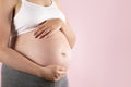 Close up of pregnant woman wearing supportive seamless maternity bra & grey yoga pants, arms on her belly. Female hands wrapped Royalty Free Stock Photo