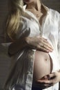 Close-up of a pregnant woman in a white shirt, gently stroking her stomach with her hands in the late stages of