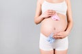 Close up of pregnant woman in white underwear holding baby pink and blue socks against her belly at gray background. Is it a boy Royalty Free Stock Photo