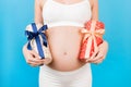 Close up of pregnant woman in white underwear holding two gift boxes at blue background. Is it a boy or a girl Childbirth