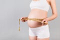 Close up of pregnant woman in white underwear measuring her growing belly at gray background. Expecting a baby. Inch measurement.