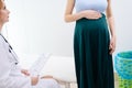 Close-up of pregnant woman holding hands on belly while sitting in tight medicine office.