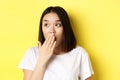 Close up of pretty asian girl looking shocked, gasping and covering mouth with hand, stare left at promotion, standing Royalty Free Stock Photo