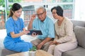 Close up pretty Asian nurse or doctor sit on sofa and use tablet to give suggestion or consult data to couple senior man and woman Royalty Free Stock Photo