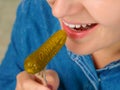 Close-up of a pretty Caucasian woman with her mouth open holding a fork with a small pickled cucumber. Front three-quarter view.