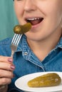 Close-up of a pretty Caucasian woman holding a fork and a plate with pickled cucumber. Front three-quarter view. Low angle view.