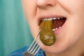 Close-up of a pretty Caucasian woman's mouth biting a pickled cucumber. Front three-quarter view. Low angle view. Indoors