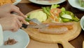 A close-up of pretty hands on the fork and knife, cut a large sausage, that was on a plate, into bite-sized pieces, and gave it to