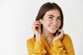 Close-up of pretty lady listening music in earphones, wearing wireless headphones and smiling, standing over white Royalty Free Stock Photo