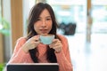 Pretty young asian female holding coffee cup, drinking morning coffee at cafe