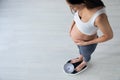 Pretty young pregnant woman standing on scales at home