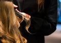 Hair straightening. Close up of pretty young woman is getting her hair equalized in beauty salon. The hairdresser is combing her