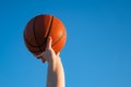 Close up of professional basketball player holding a ball in the hand. Street basketball athlete with a ball and blue sky in the