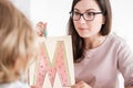 Close-up of a professional child development therapist showing a prop picture of letter `m` to a kid during a meeting.